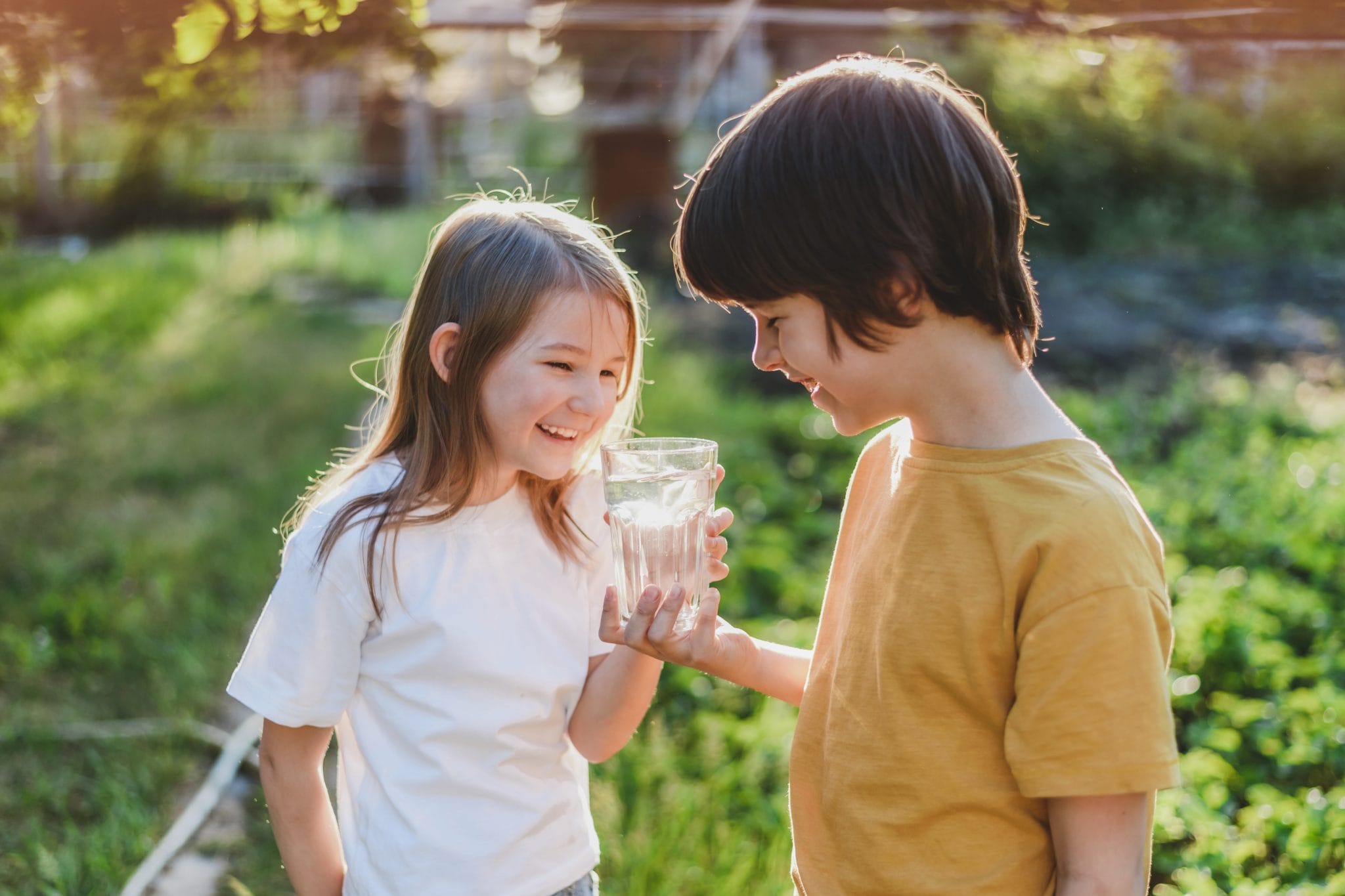 A boy and a girl drink water from a glass in nature on a sunny day